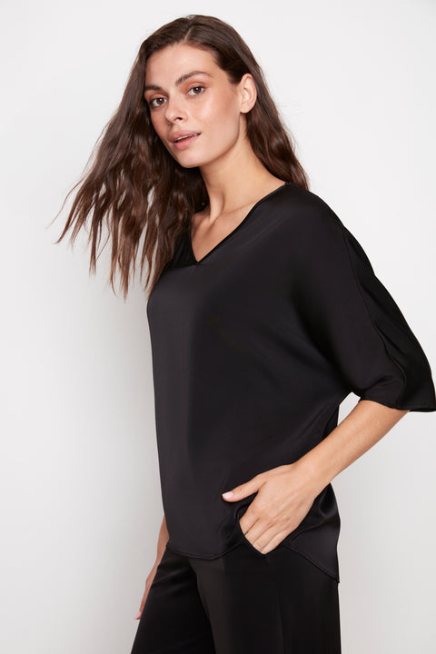 Side view of model wearing UP! Belize Satin V-Neck Short Sleeve Top in Black with dolman sleeve detail.
