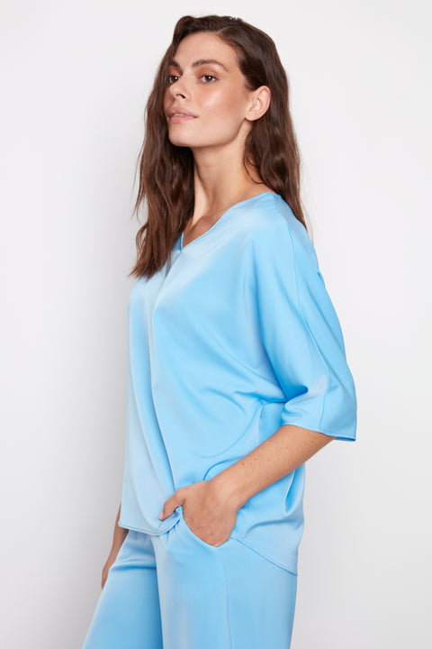 Side view of model wearing UP! Belize Satin V-Neck Short Sleeve Top in Celeste Blue with dolman sleeve detail.
